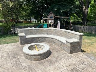 Curved stone fire pit seating in a park playground area with trees and a swing set nearby