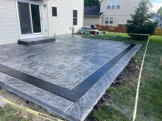Backyard concrete patio with dark border beside a white house
