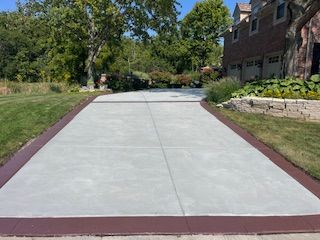 New concrete driveway bordered by grass and trees beside a brick house