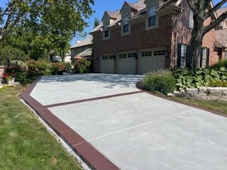 Brick house with three-car garage and a wide concrete driveway bordered by red trim and grass