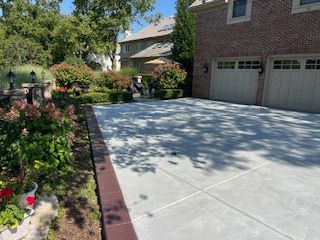 Driveway beside a brick house with garage, garden beds, and trees in bright sunlight
