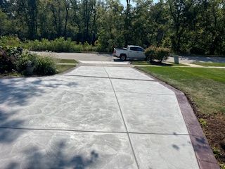 Concrete driveway curving toward a road, with a white pickup truck and trees in the background.