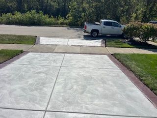 Concrete driveway leading to a street, with a white pickup truck parked across the road.