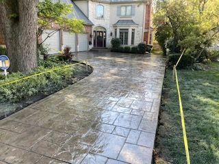 Wet stone walkway leading to a house entrance beside a landscaped yard with trees and shrubs