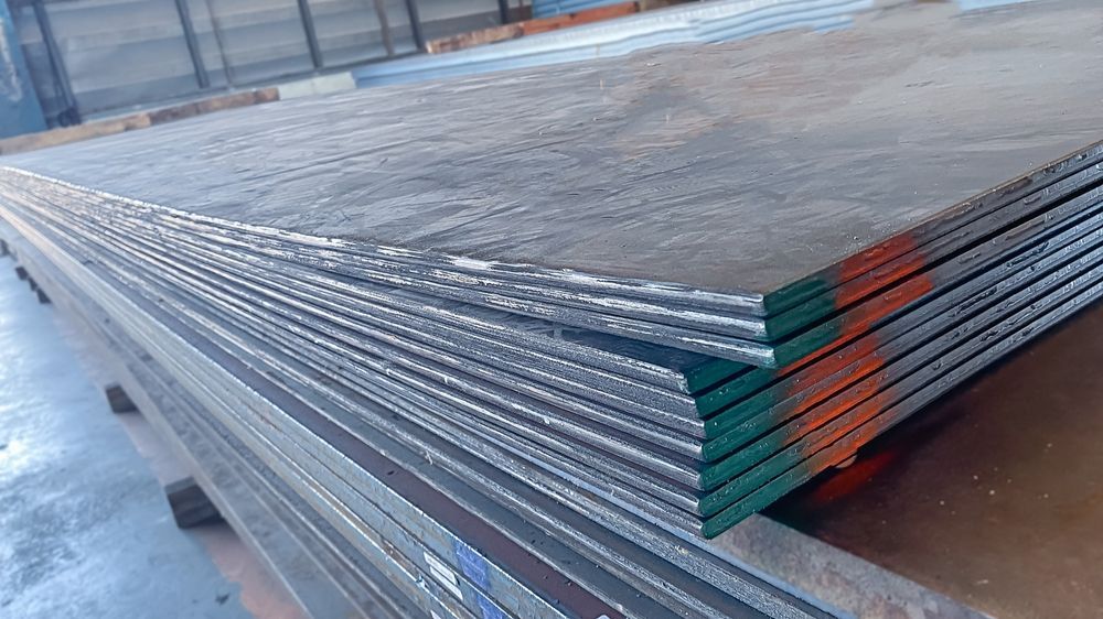 Stacked metal sheets bound with green and orange straps in an industrial yard.