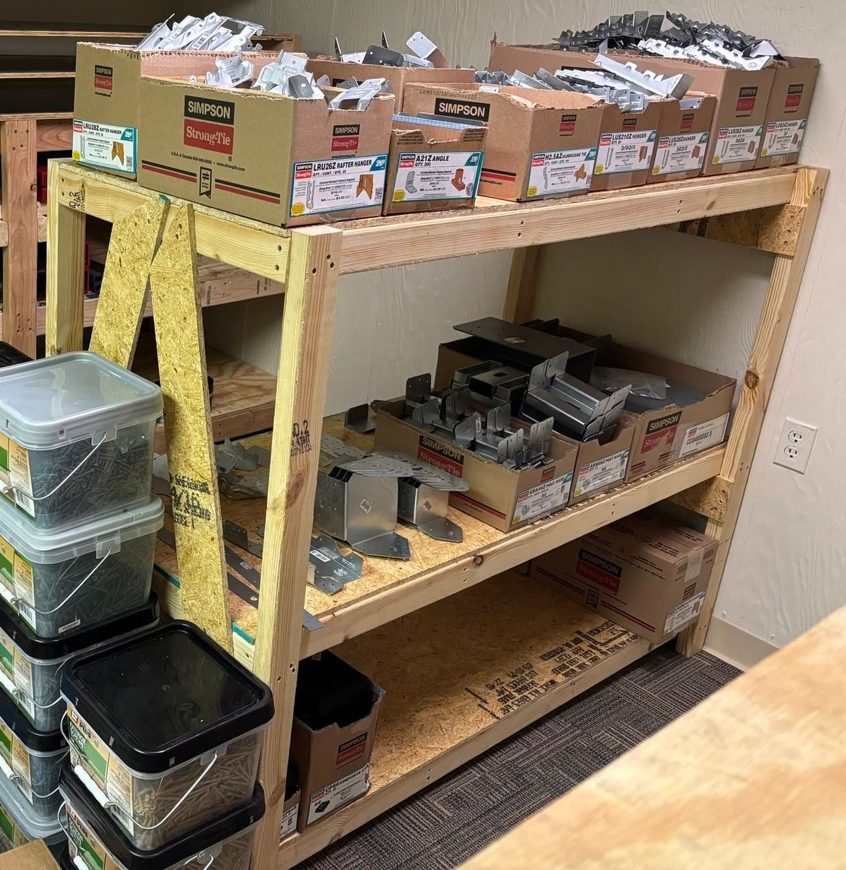 Workshop shelf with labeled cardboard boxes and stacked plastic bins holding small parts and tools.