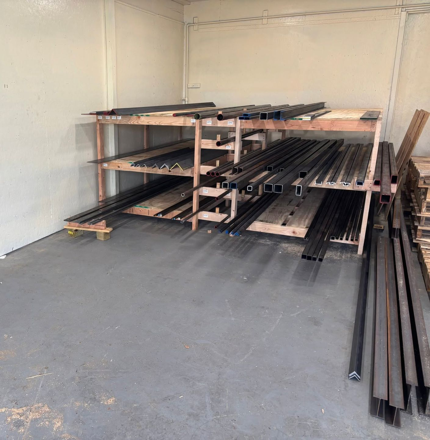 Metal pipes and wooden planks stacked on shelving in a bare storage room