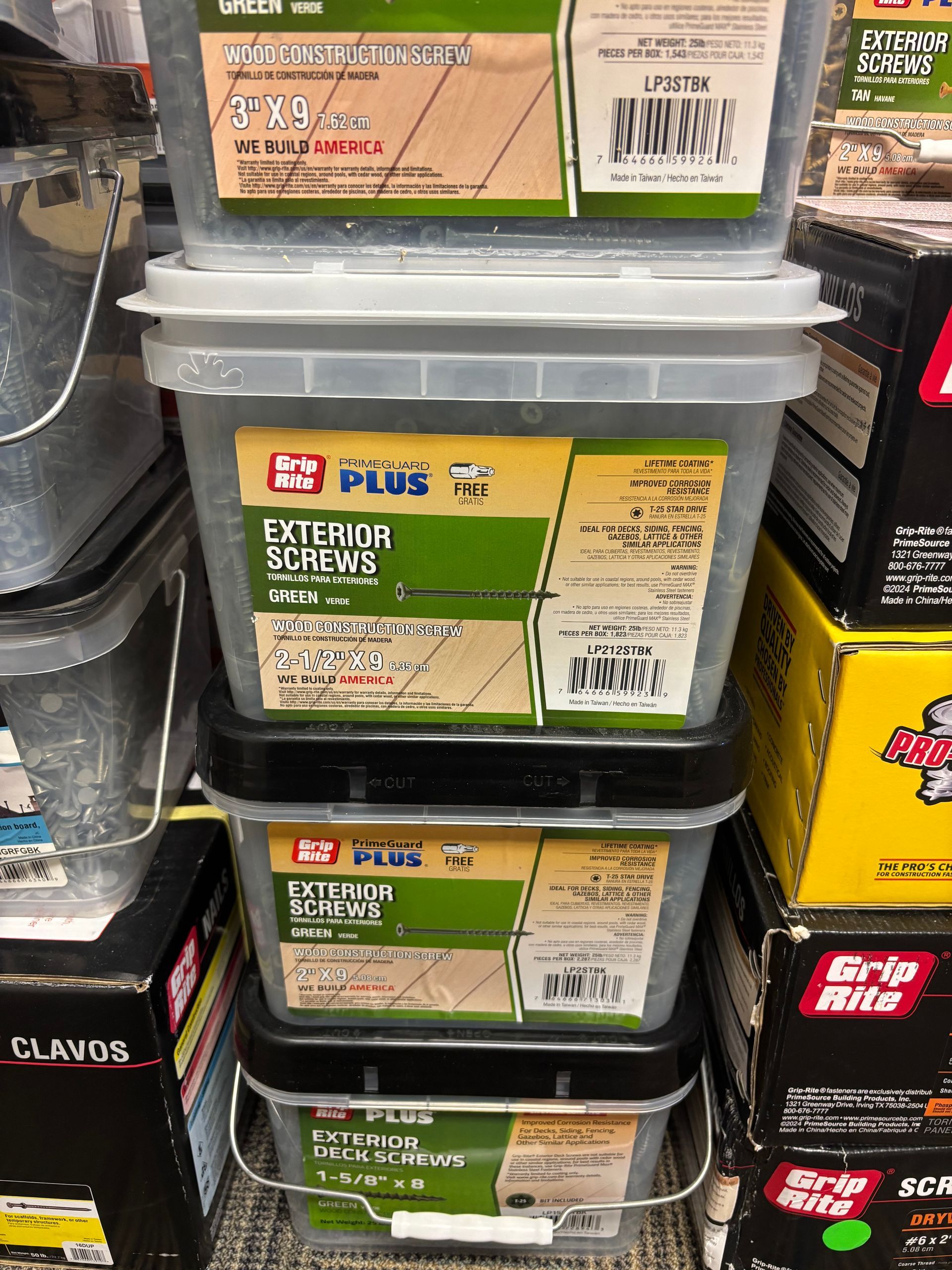 Stacked plastic storage boxes with green labels on a store shelf, beside other hardware containers.