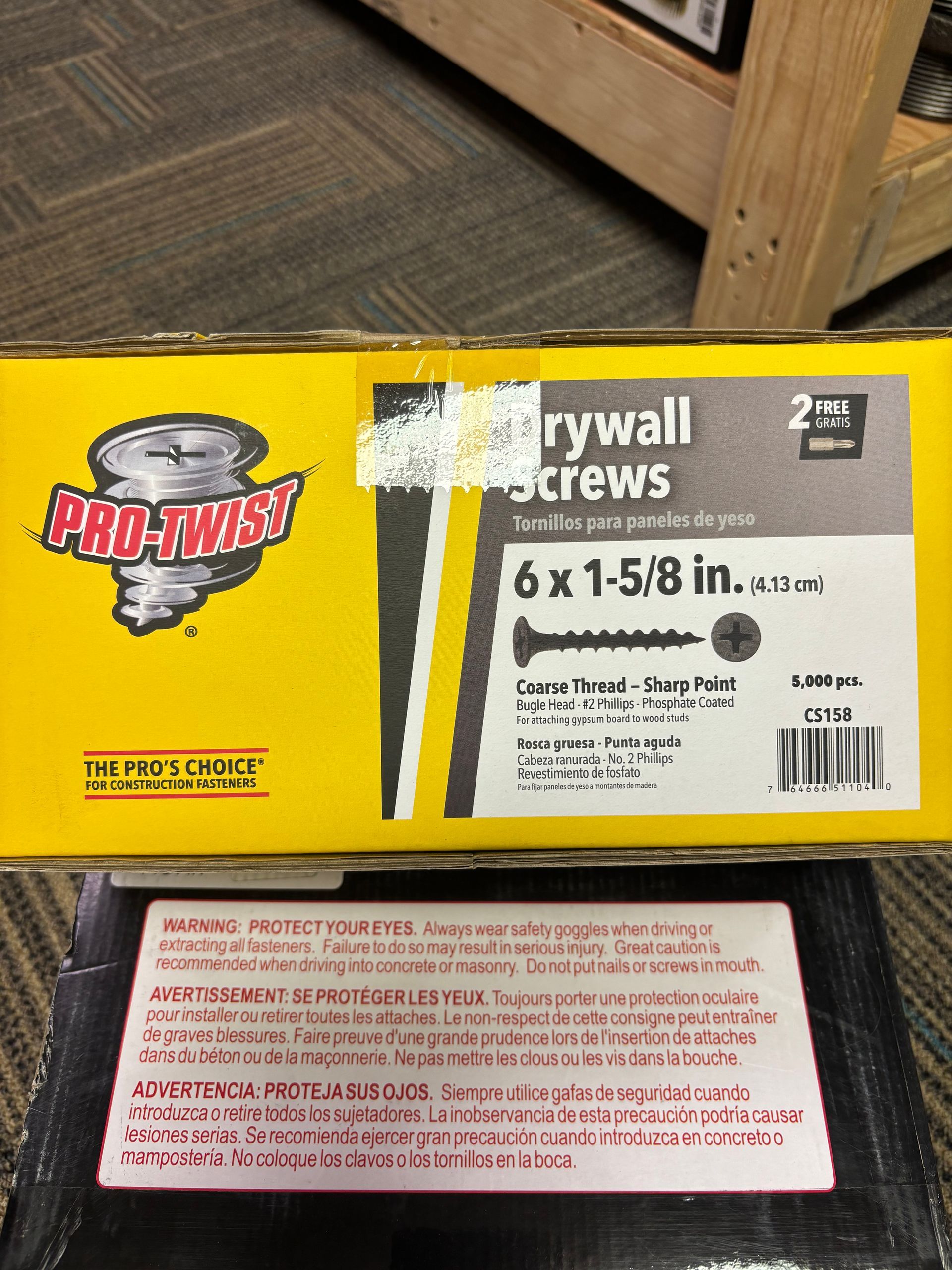 Box of Pro-Twist drywall screws on carpeted floor, with a safety warning label below.