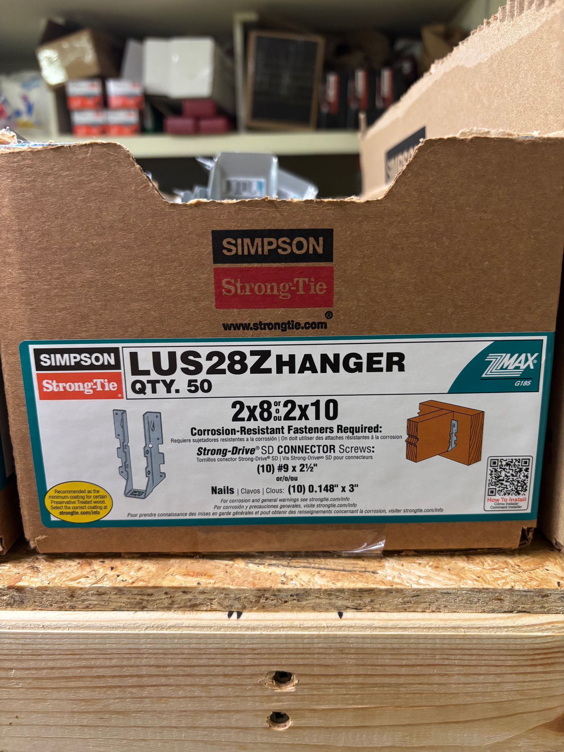 Cardboard box of Simpson Strong-Tie LU28 hanger connectors on a wooden workbench.