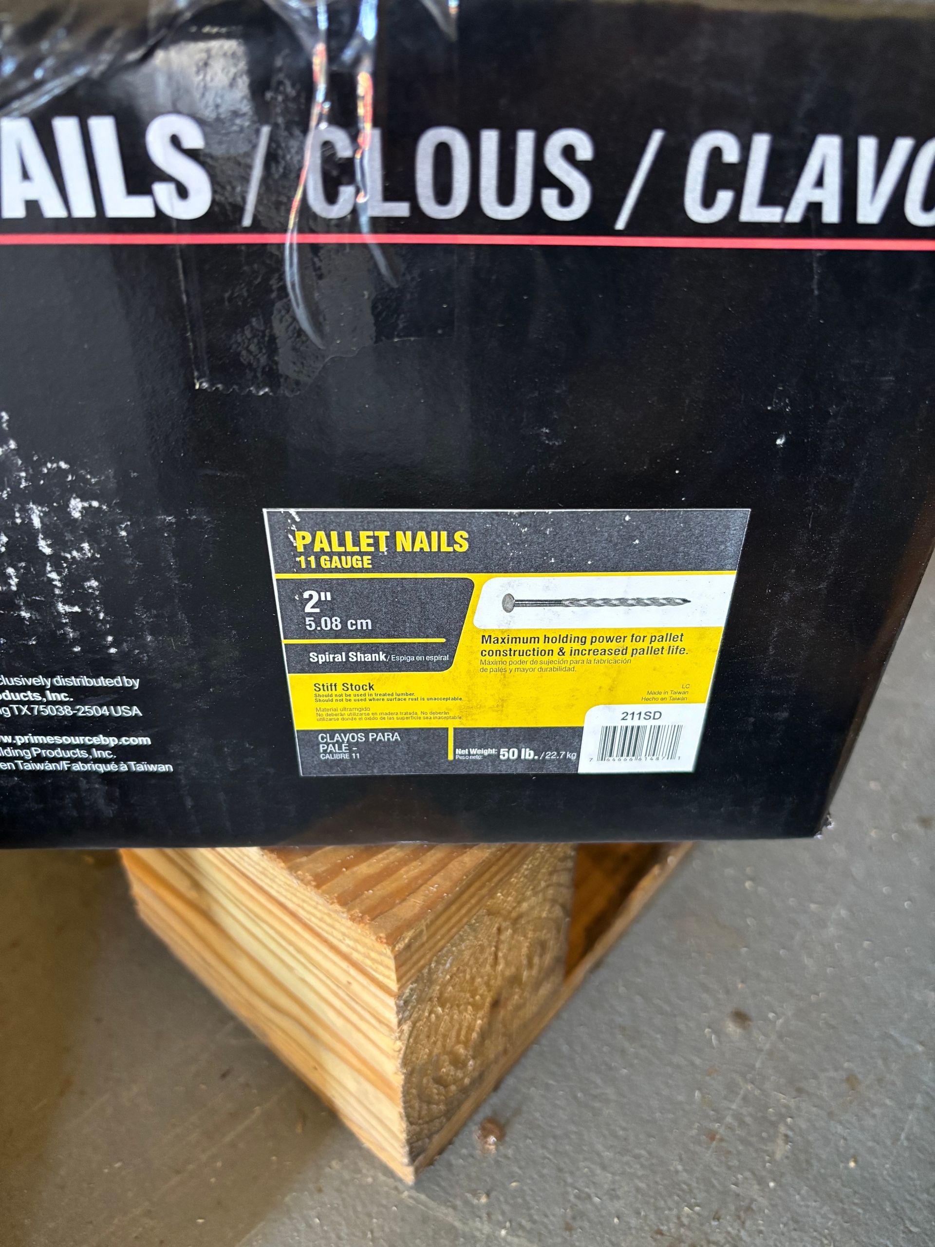 Black box labeled “NAILS / CLOUS / CLAV…” with a yellow product sticker on a wooden pallet