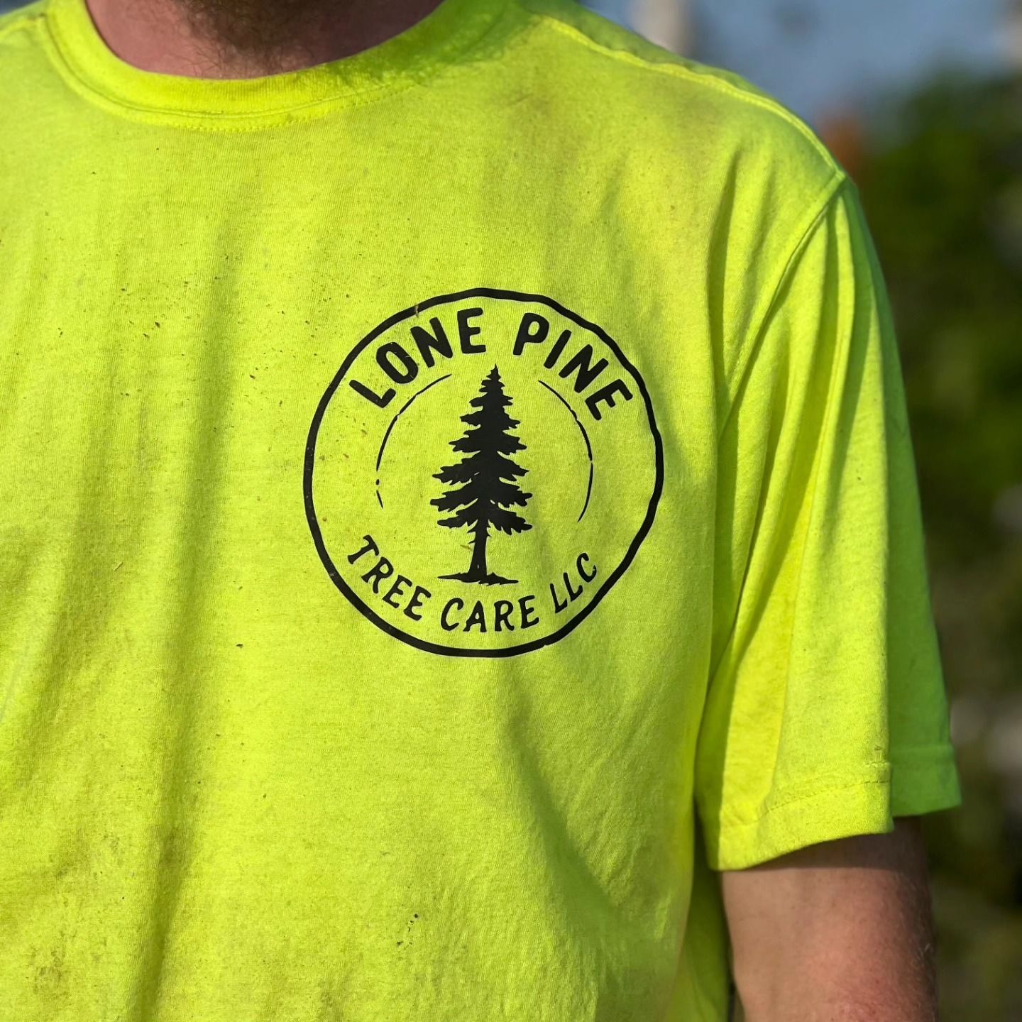 A person wearing a neon yellow t-shirt with a black circular logo that reads 
