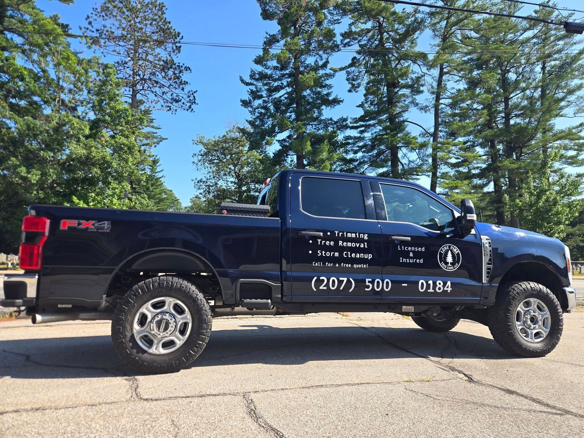 A blue Ford F-250 pickup truck with company branding and a phone number on its side, parked on an asphalt lot.