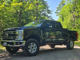 A black Ford Super Duty pickup truck parked on a dirt road in a wooded area.