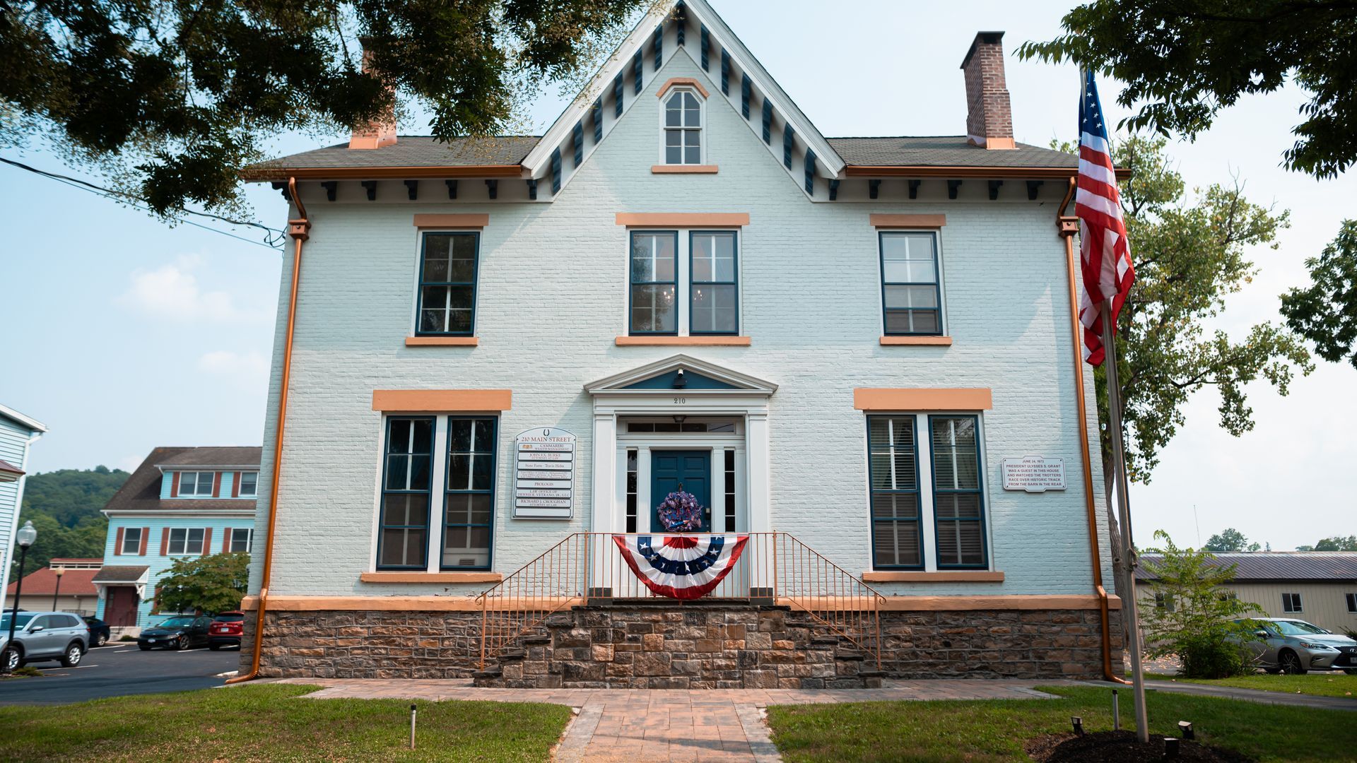 Two-story white building with US flag, decorated with patriotic garland.