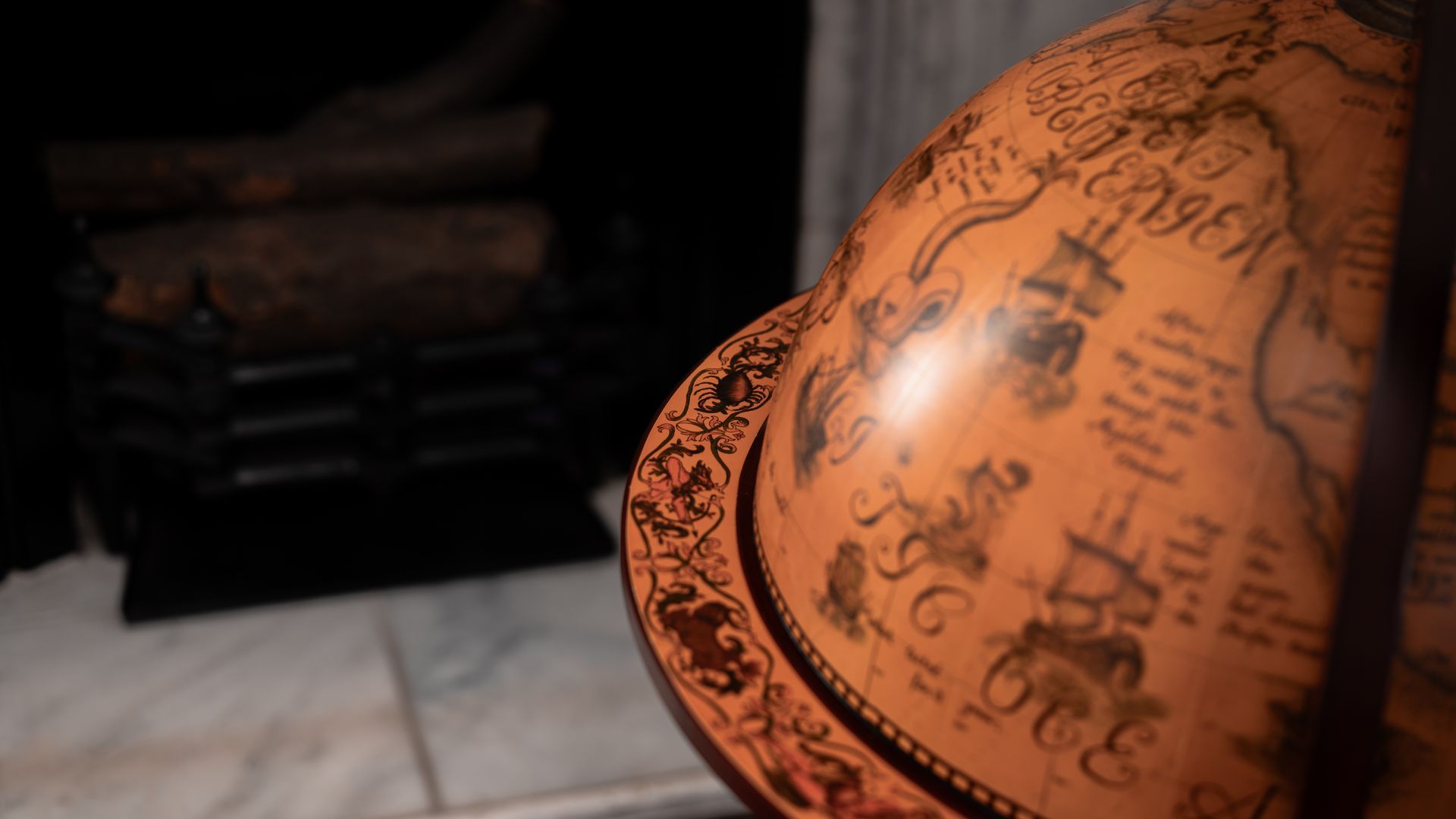Antique globe with map details, near a fireplace with logs.
