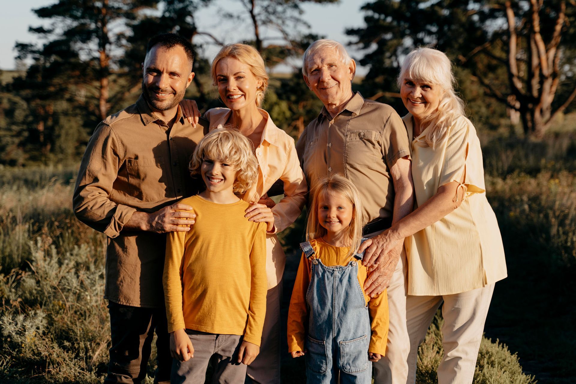 Family portrait outdoors. Six people, smiling. Sunlight, field of tall grass.