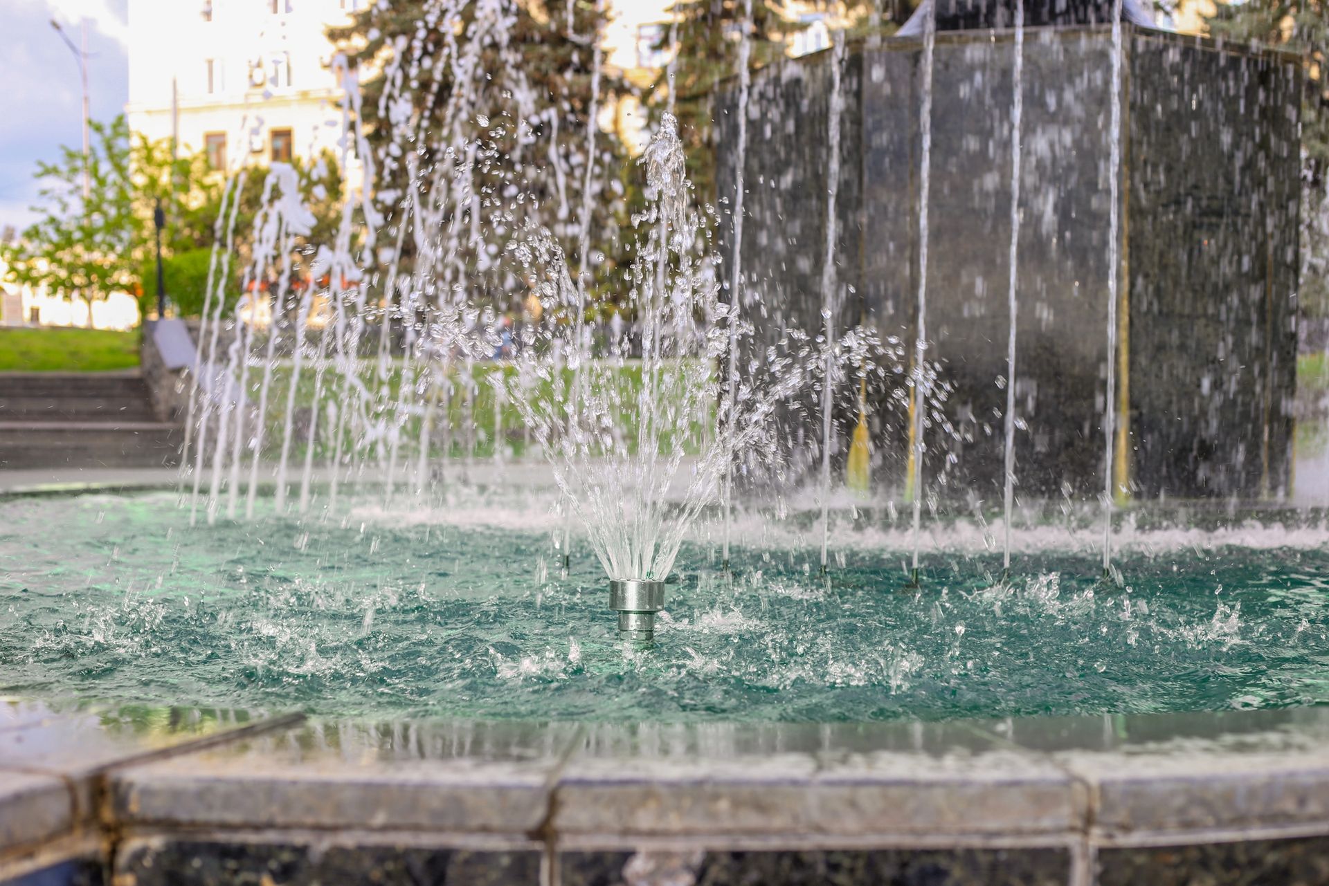 A fountain is spraying water in a park on a sunny day.