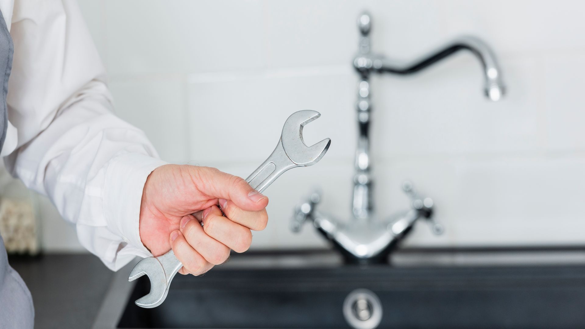 A person is holding a wrench in front of a sink.
