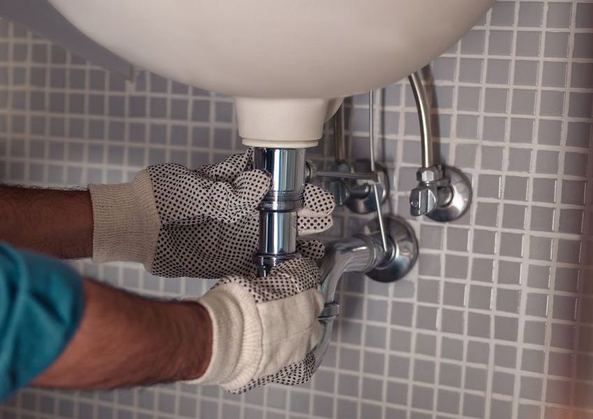 A person is fixing a sink in a bathroom.