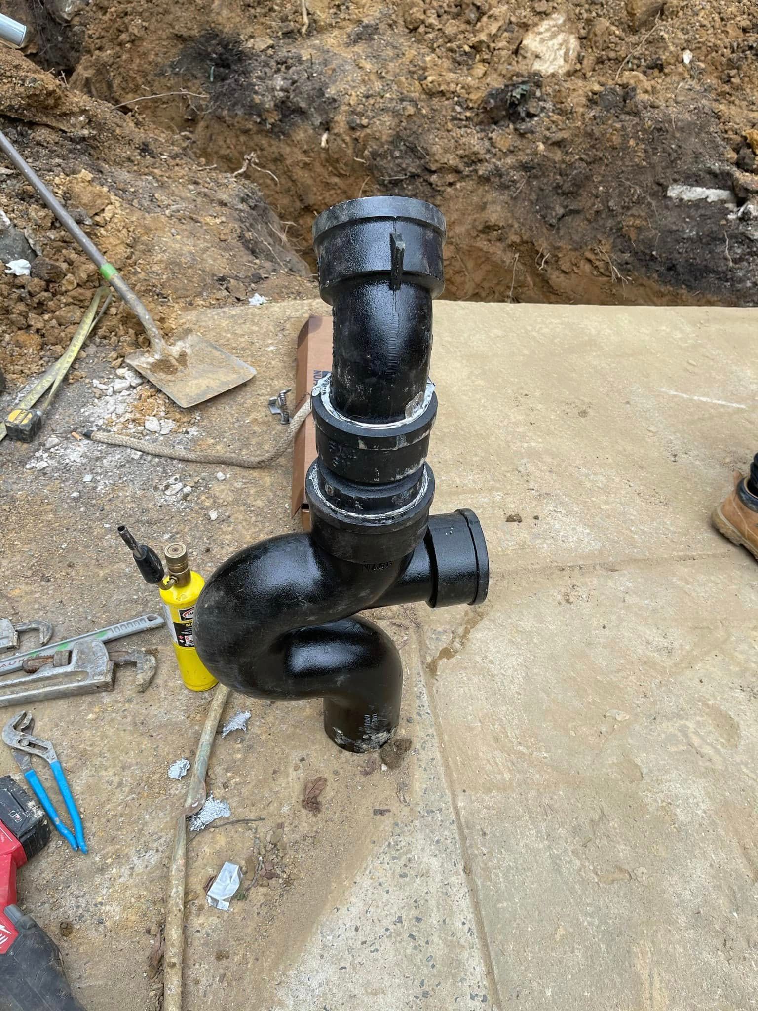 A black pipe is being installed in a hole in the ground.