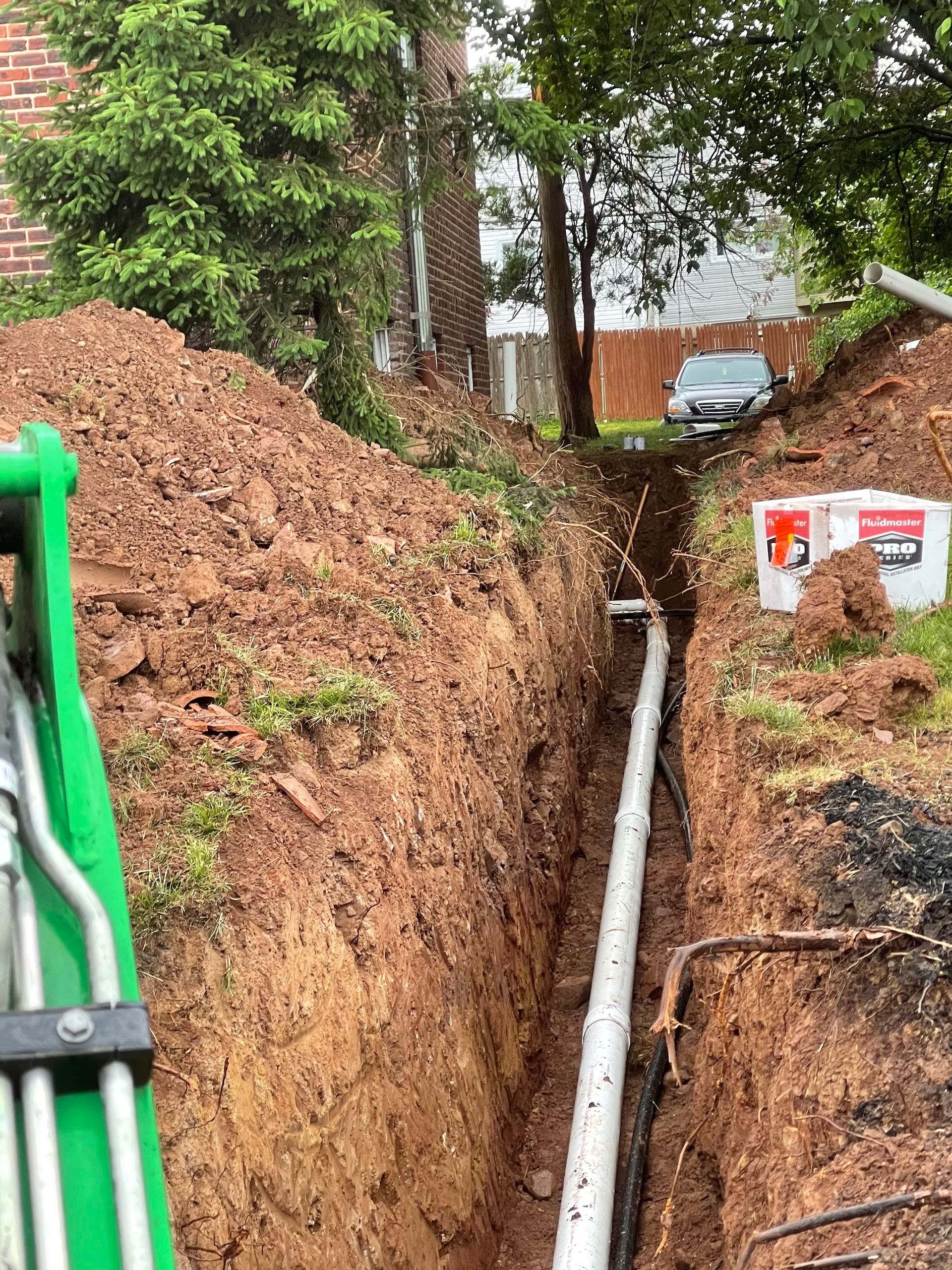 A green tractor is digging a trench with a pipe in it.