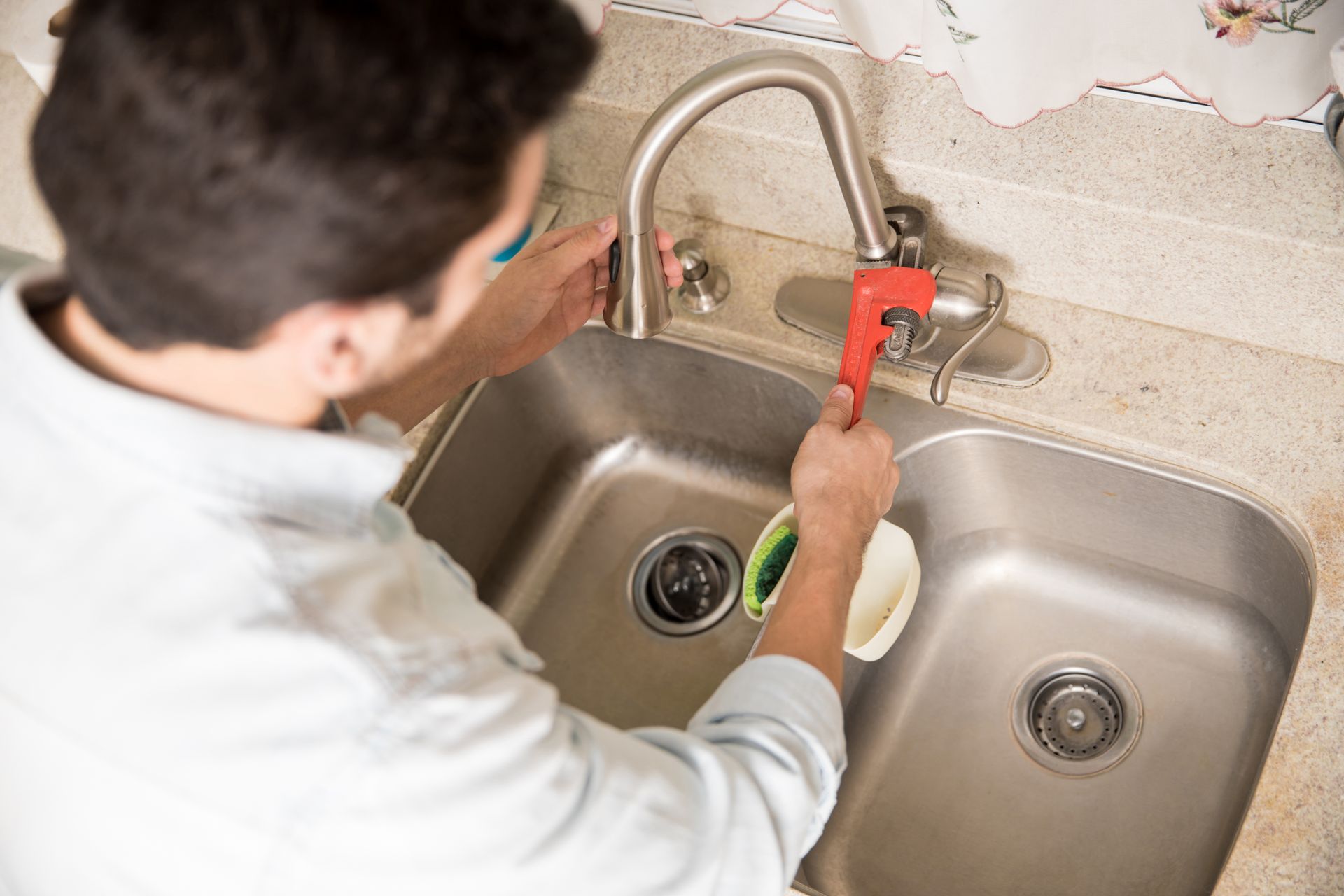 A man is cleaning a kitchen sink with a wrench.