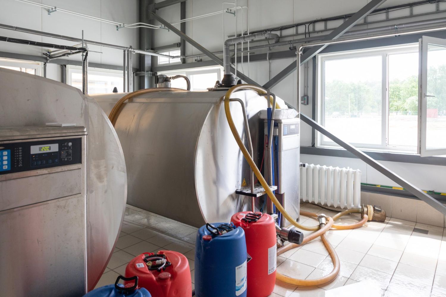 Large stainless steel tanks inside a factory with blue, red, and orange containers on the floor.