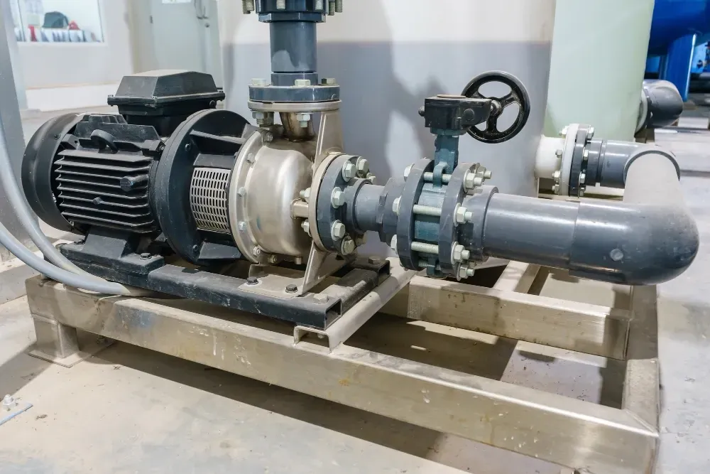 Industrial pump and motor assembly mounted on a concrete base in a workshop.