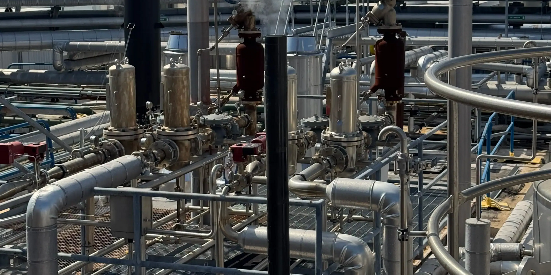 A high-angle view of industrial piping, valves, and metallic equipment at a processing facility.