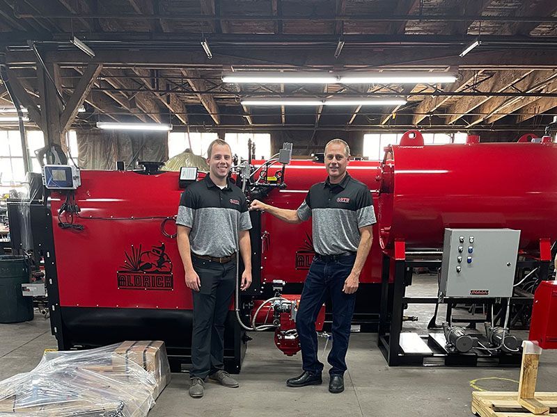 Two men are standing next to each other in front of a red machine in a factory in Miami, FL.