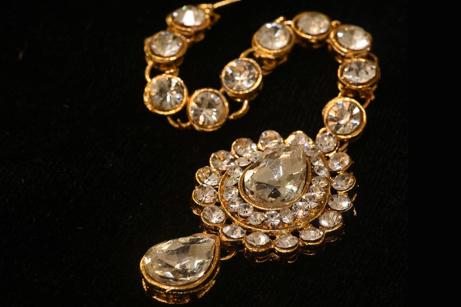 Gold and diamond maang tikka, ornate headpiece with a large central gem, on a black surface.