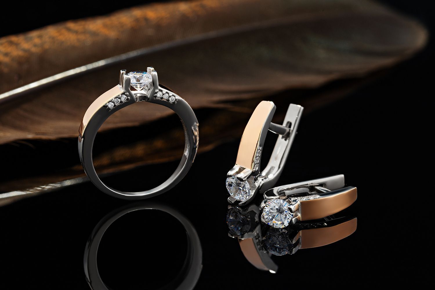 Ring and earrings with diamonds and gold accents on a black surface with a feather.