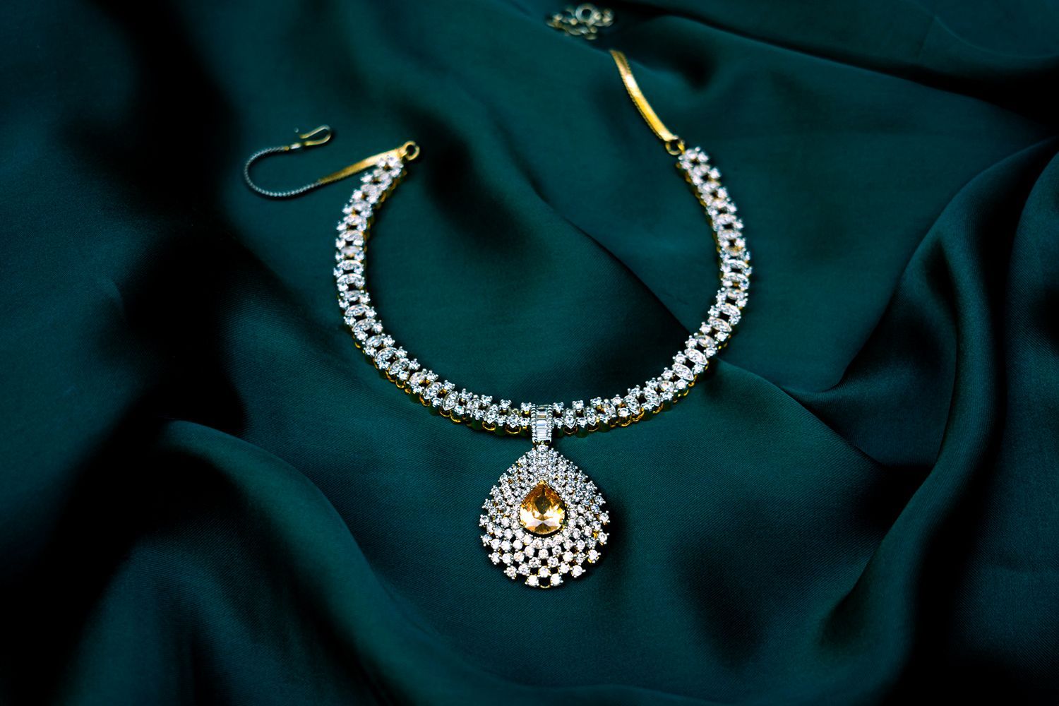 Diamond necklace with a pear-shaped gemstone pendant on a dark green fabric. Diamond necklace with a pear-shaped gemstone pendant on a dark green fabric.