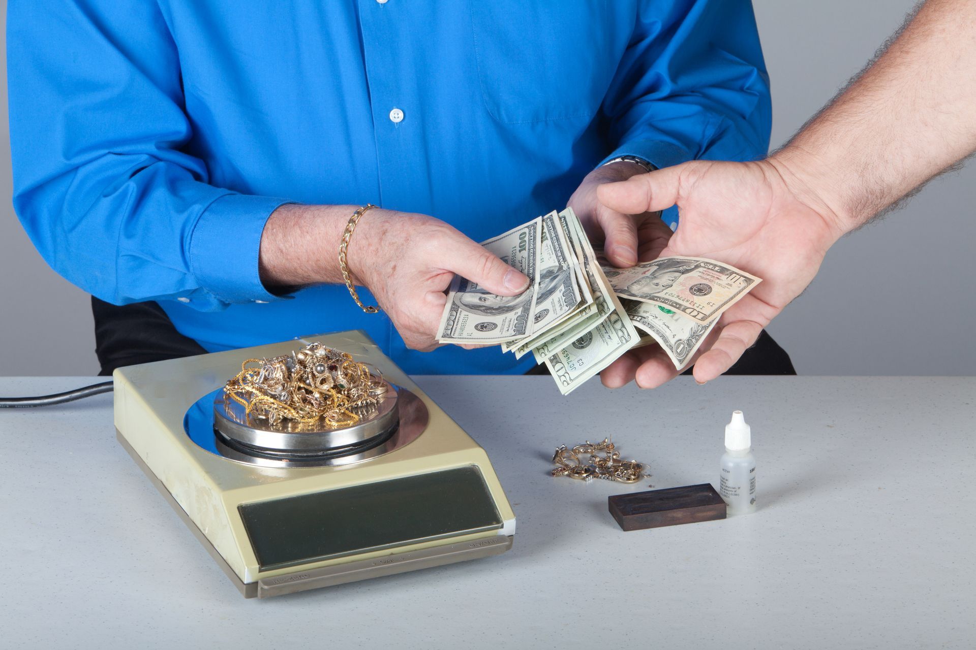 Person in blue shirt exchanges cash for gold jewelry on a scale Person in blue shirt exchanges cash for gold jewelry on a scale