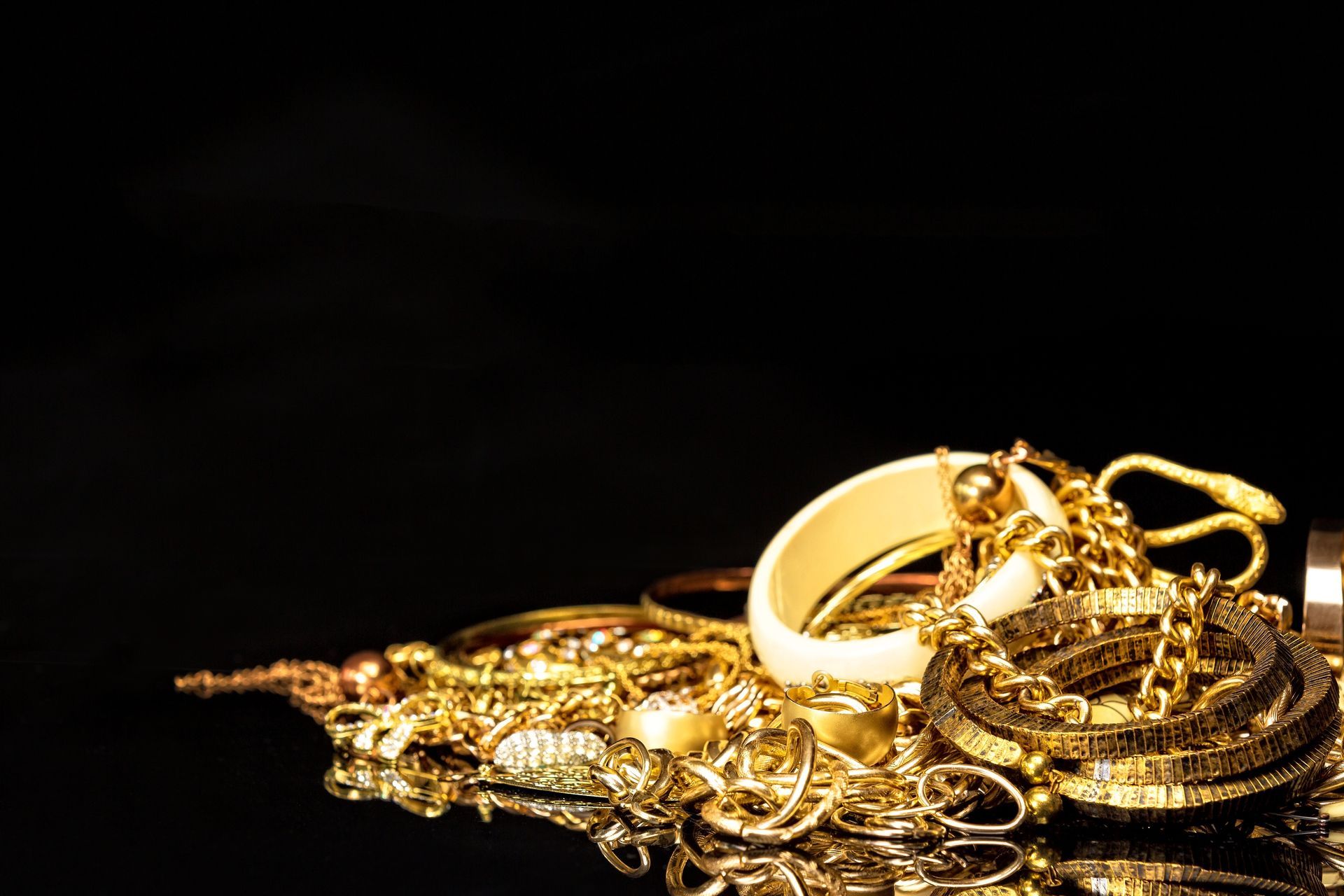 Gold jewelry piled on a dark reflective surface, including rings, chains, and bracelets. Gold jewelry piled on a dark reflective surface, including rings, chains, and bracelets.