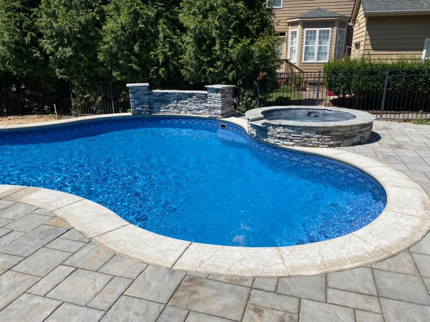 Backyard swimming pool with blue water, stone deck, and hot tub beside a house