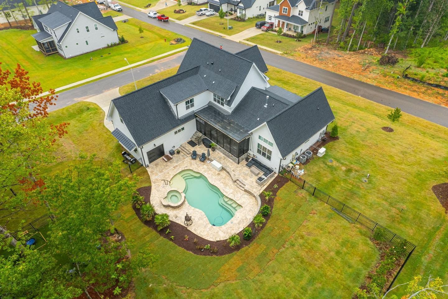 Aerial view of a large gray-roofed house with a backyard pool and patio on a grassy lot.