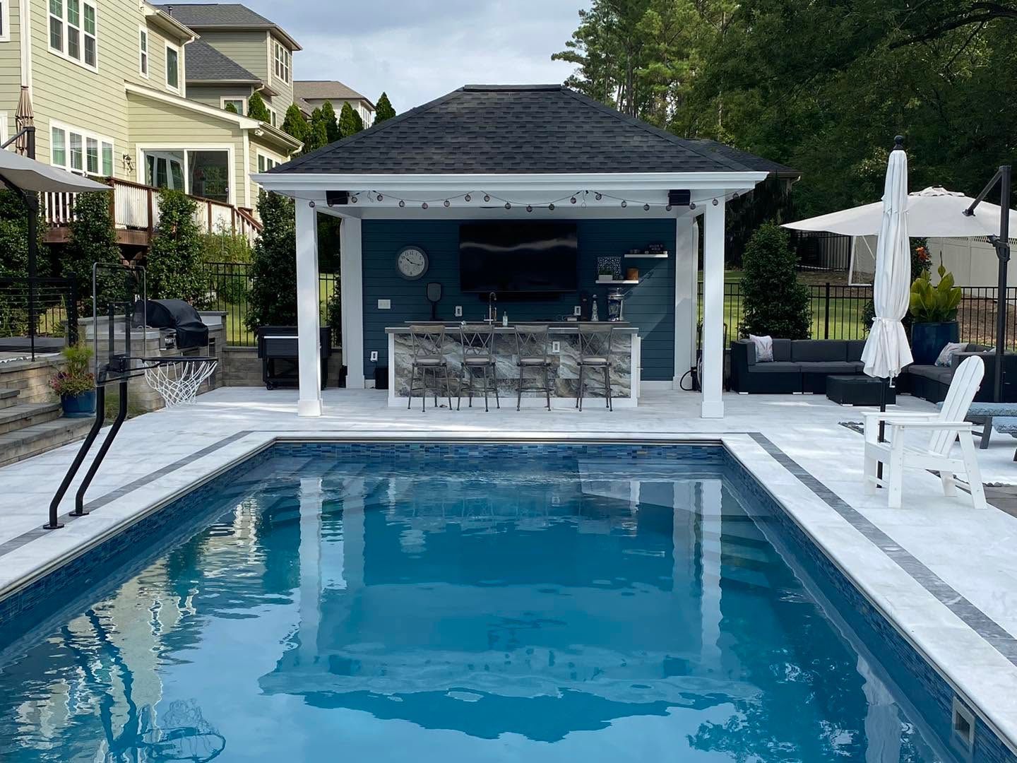 Modern backyard pool with lounge chairs, white stone deck, and gray cloudy sky