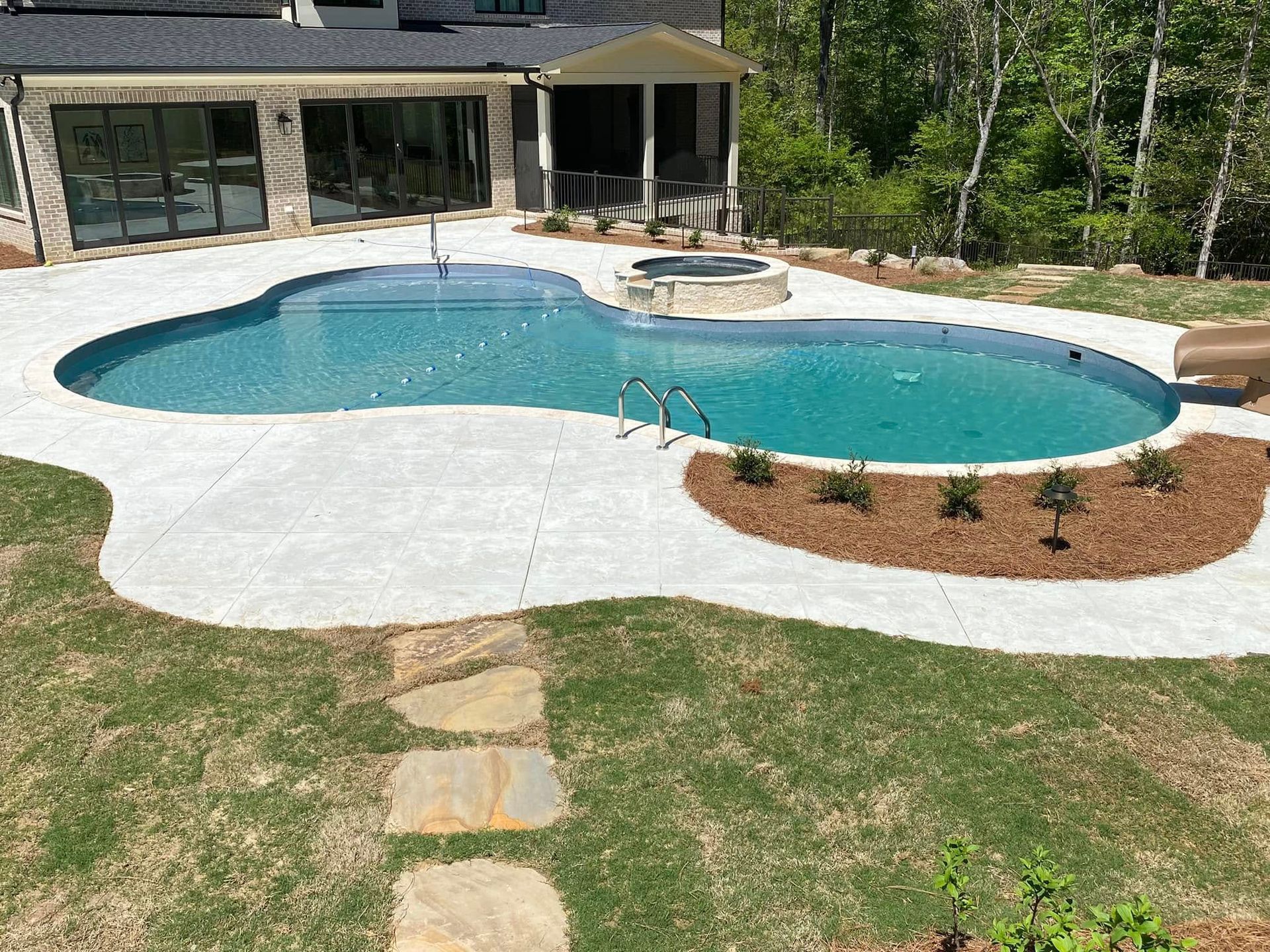 Backyard pool with a stone deck, hot tub, and landscaped lawn beside a house