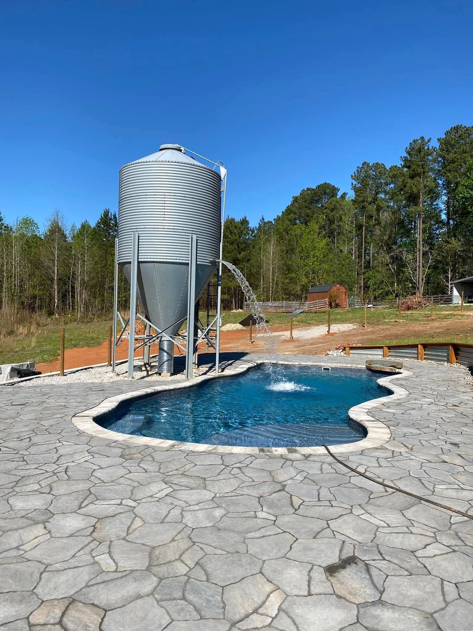 Outdoor pool with stone deck and a tall silver water tank under a clear blue sky