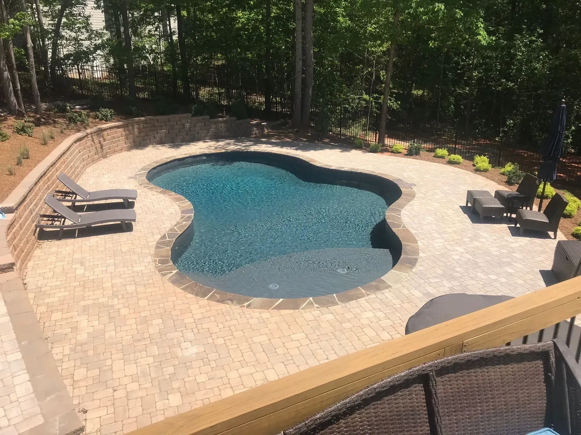 Backyard swimming pool with brick patio, lounge chairs, and surrounding trees