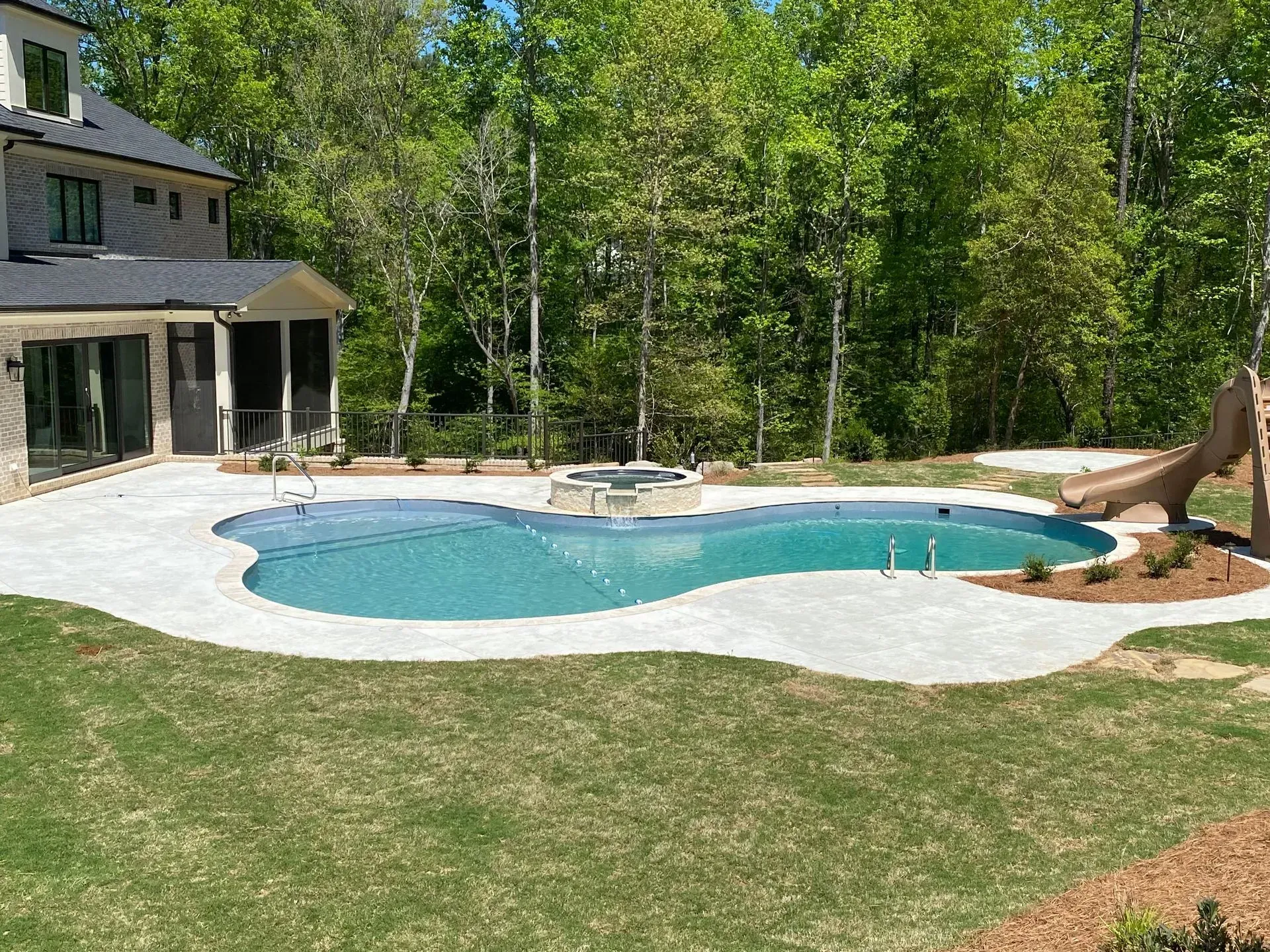 Backyard with a swimming pool, patio, and house beside a wooded area