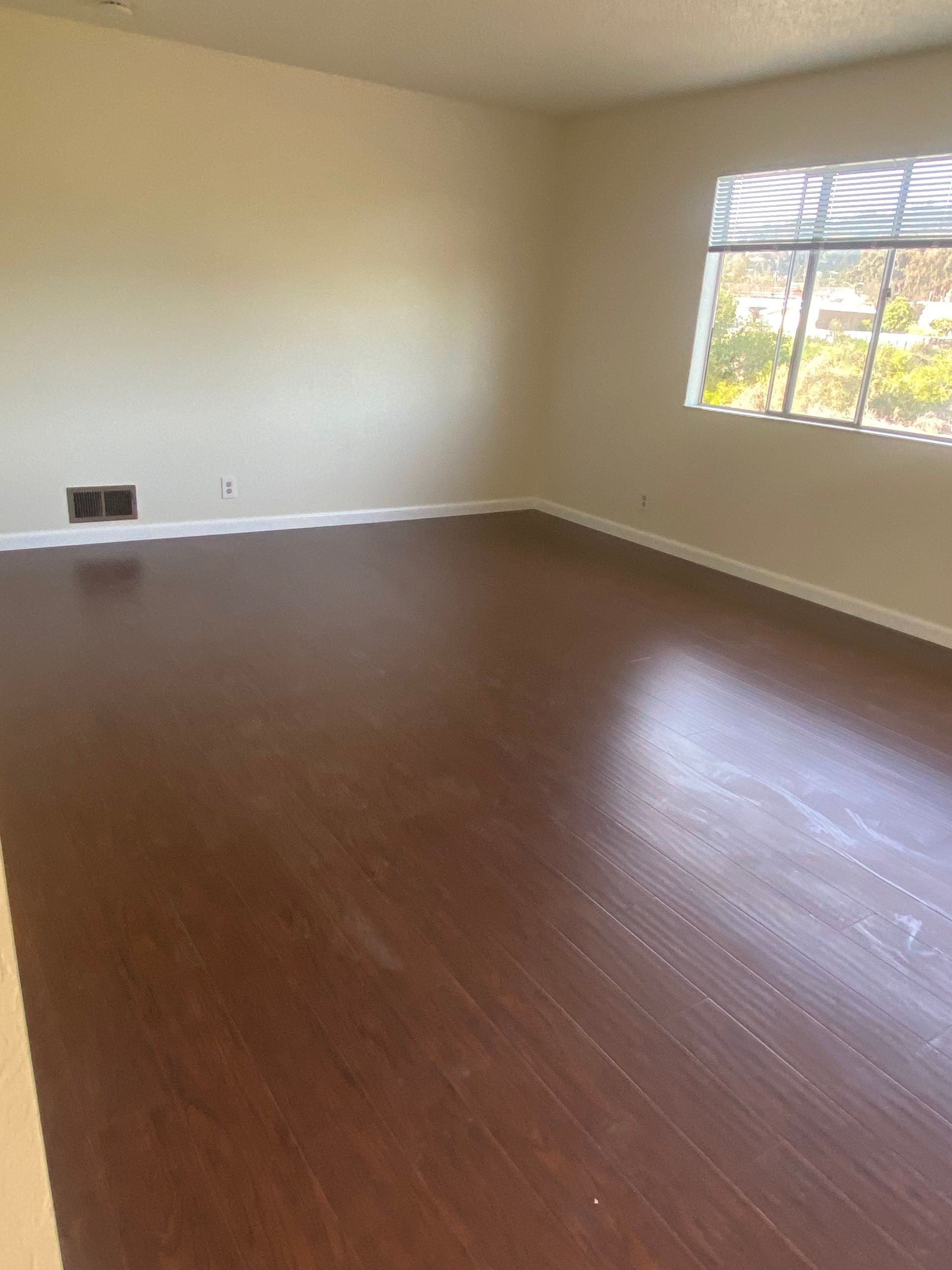 Empty beige room with brown wood floor and a window letting in sunlight.