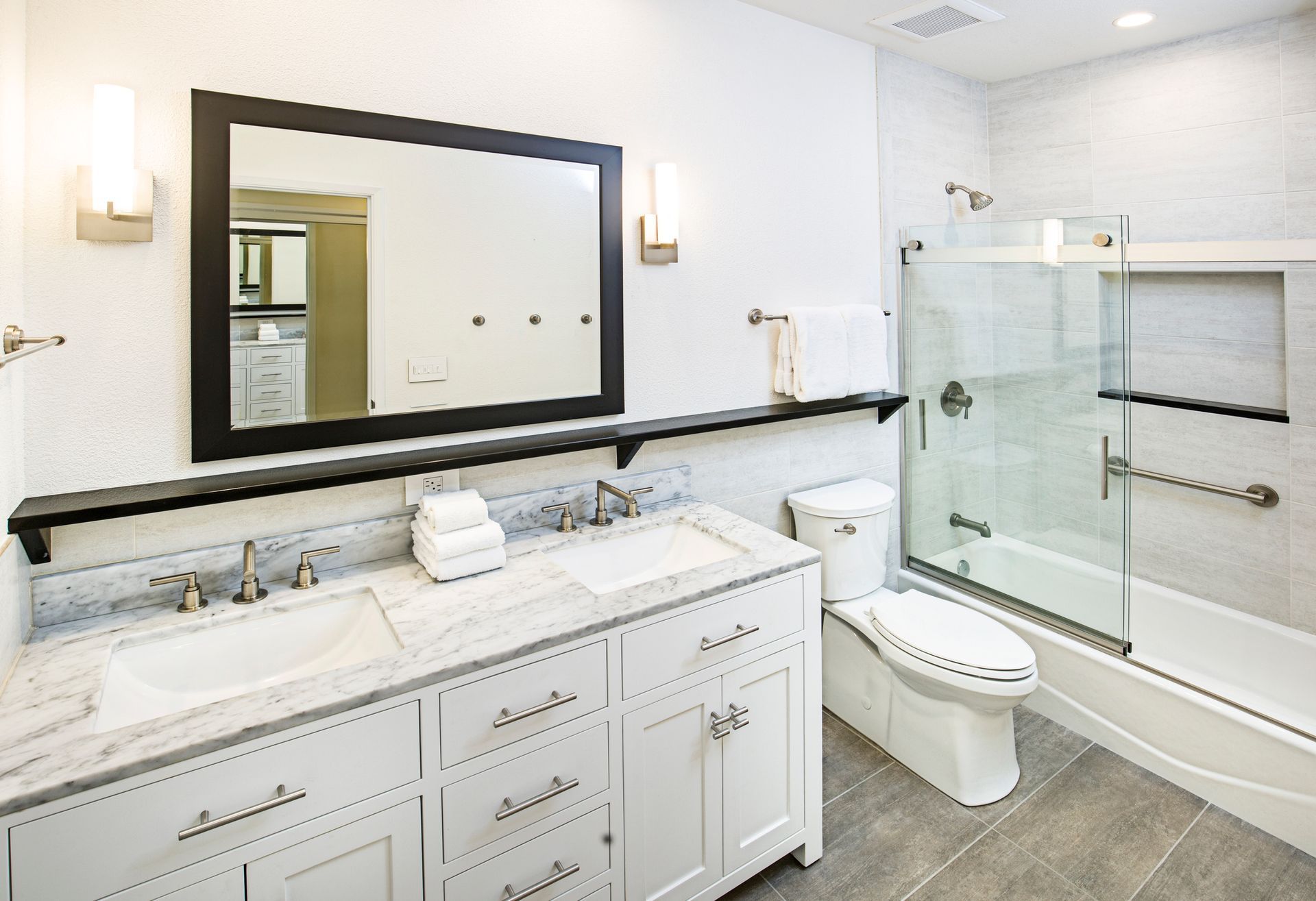 Bright modern bathroom with twin sinks, freestanding tub, and glass shower with beige tile.