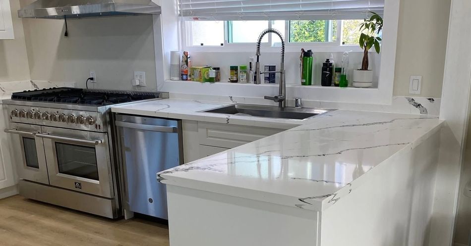 Modern kitchen with stainless steel stove, sink, white cabinets, and large marble island