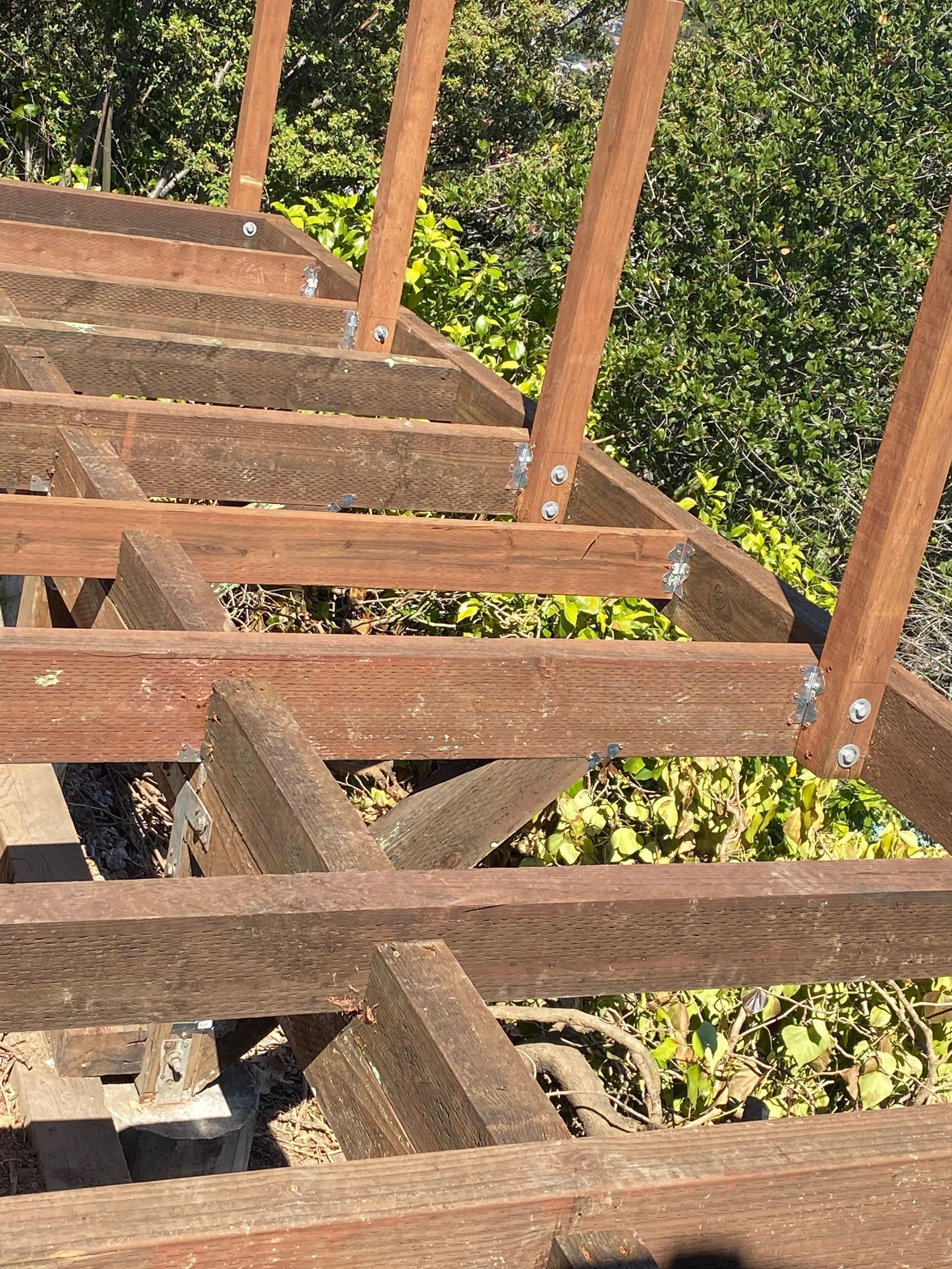 Wooden ramp or walkway under construction beside green foliage, with metal rail posts and beams.