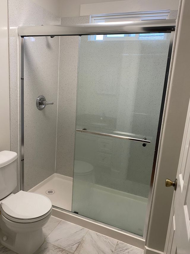 Small bathroom with toilet and glass shower enclosure with frosted sliding door.