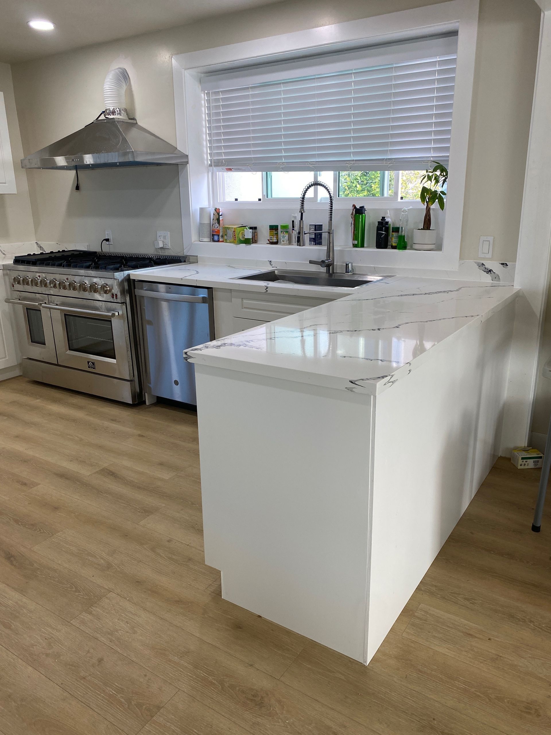 Bright modern kitchen with white cabinets, stainless stove, island, and window above the sink