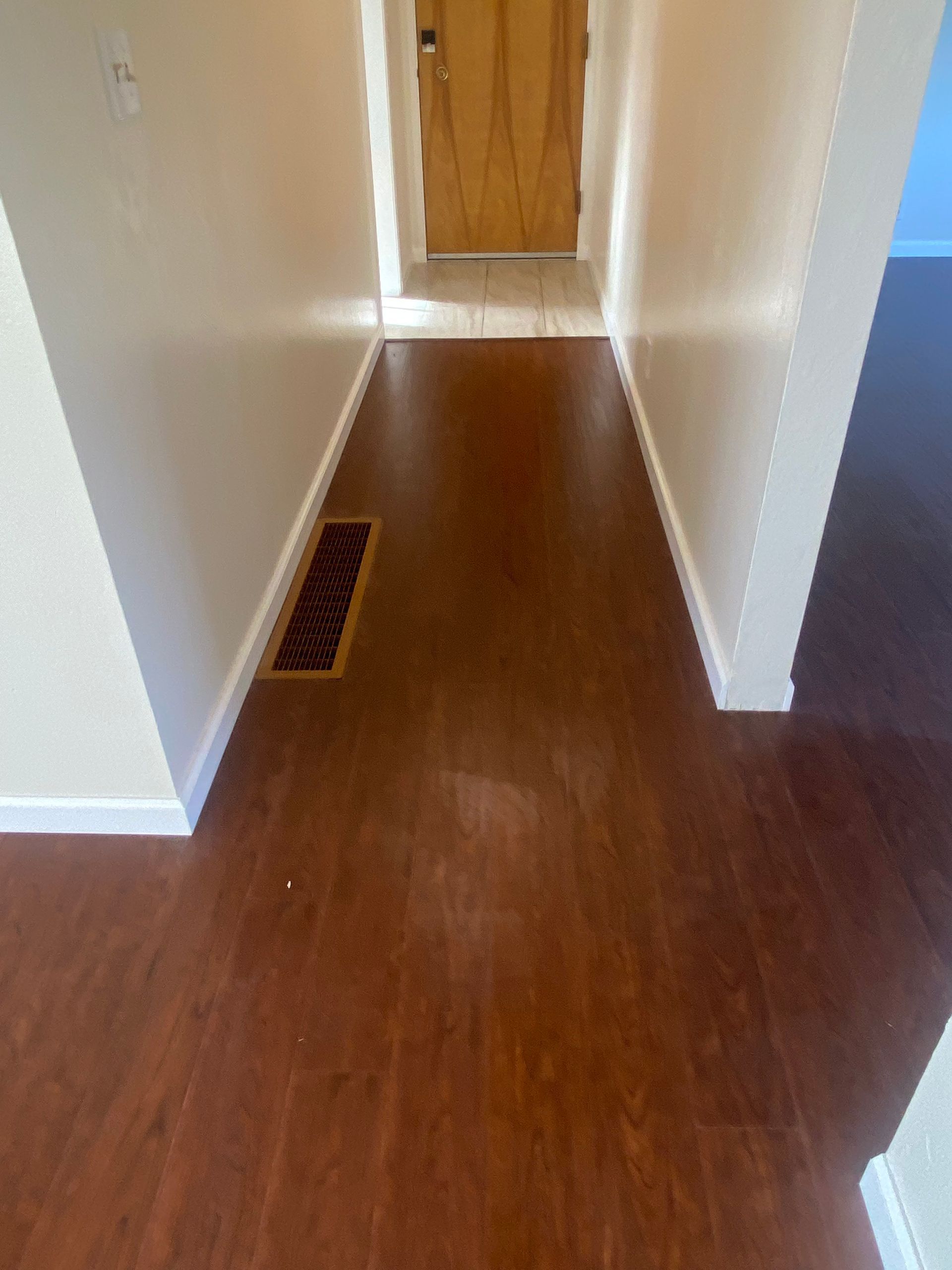 Empty hallway with brown wood flooring, white walls, and a closed wooden door at the end.